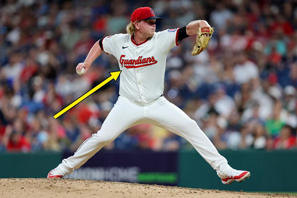 Baseball player mid-pitch on the field, wearing a uniform with "Guardians" on the jersey, in front of a blurred crowd backdrop