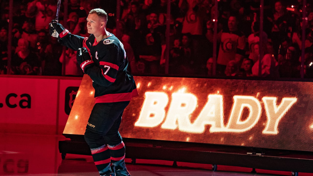 A hockey player representing the Ottawa Senators skates in front of an electronic sign reading