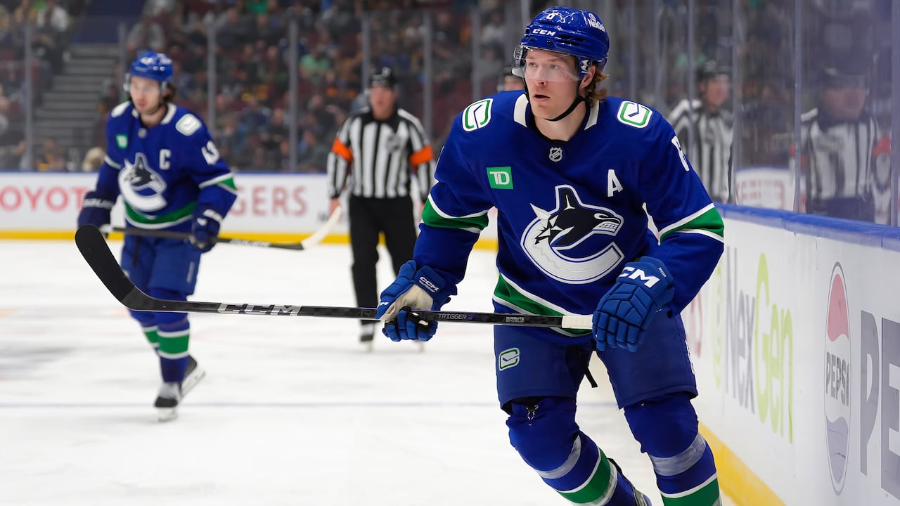 A male ice hockey player skates near the boards with both hands on his stick.