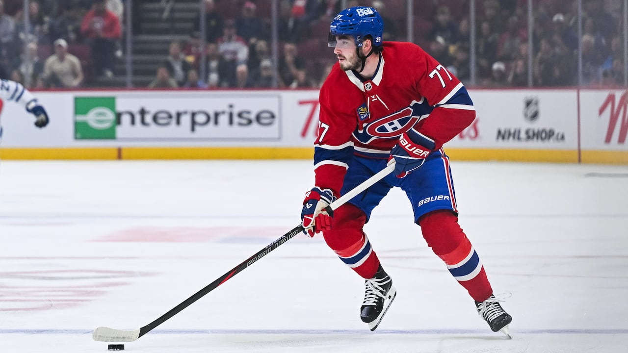 A hockey player, male, directs his gaze rightward while advancing with the puck.