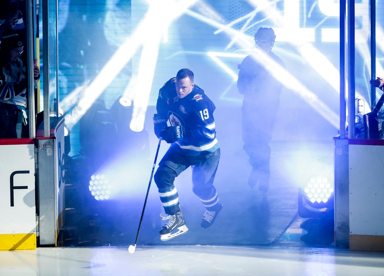 A hockey player jumps onto the ice while spotlights shine on him.