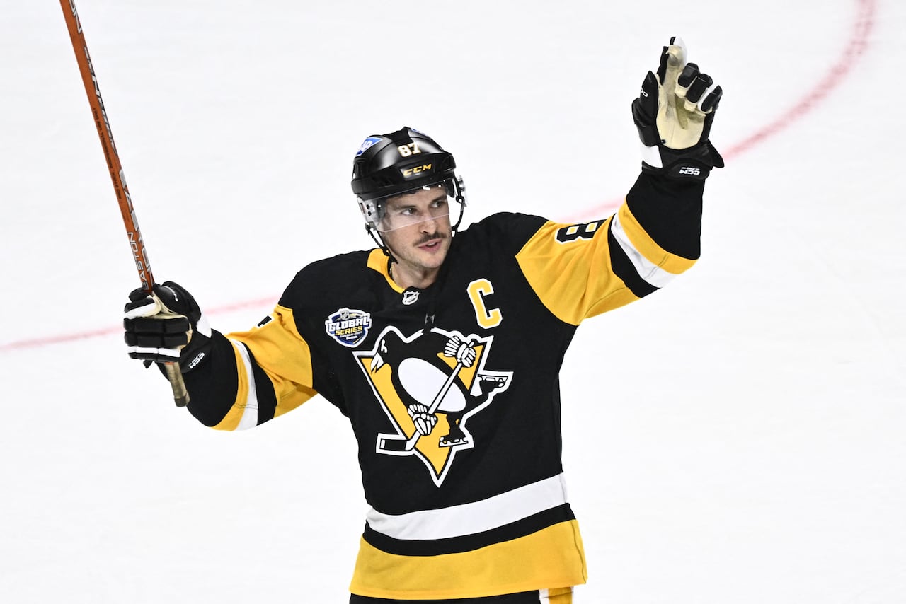 A hockey player wearing a white, black and yellow jersey gestures to the crowd.