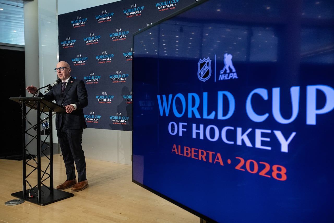 A man presenting from a podium next to a display screen.