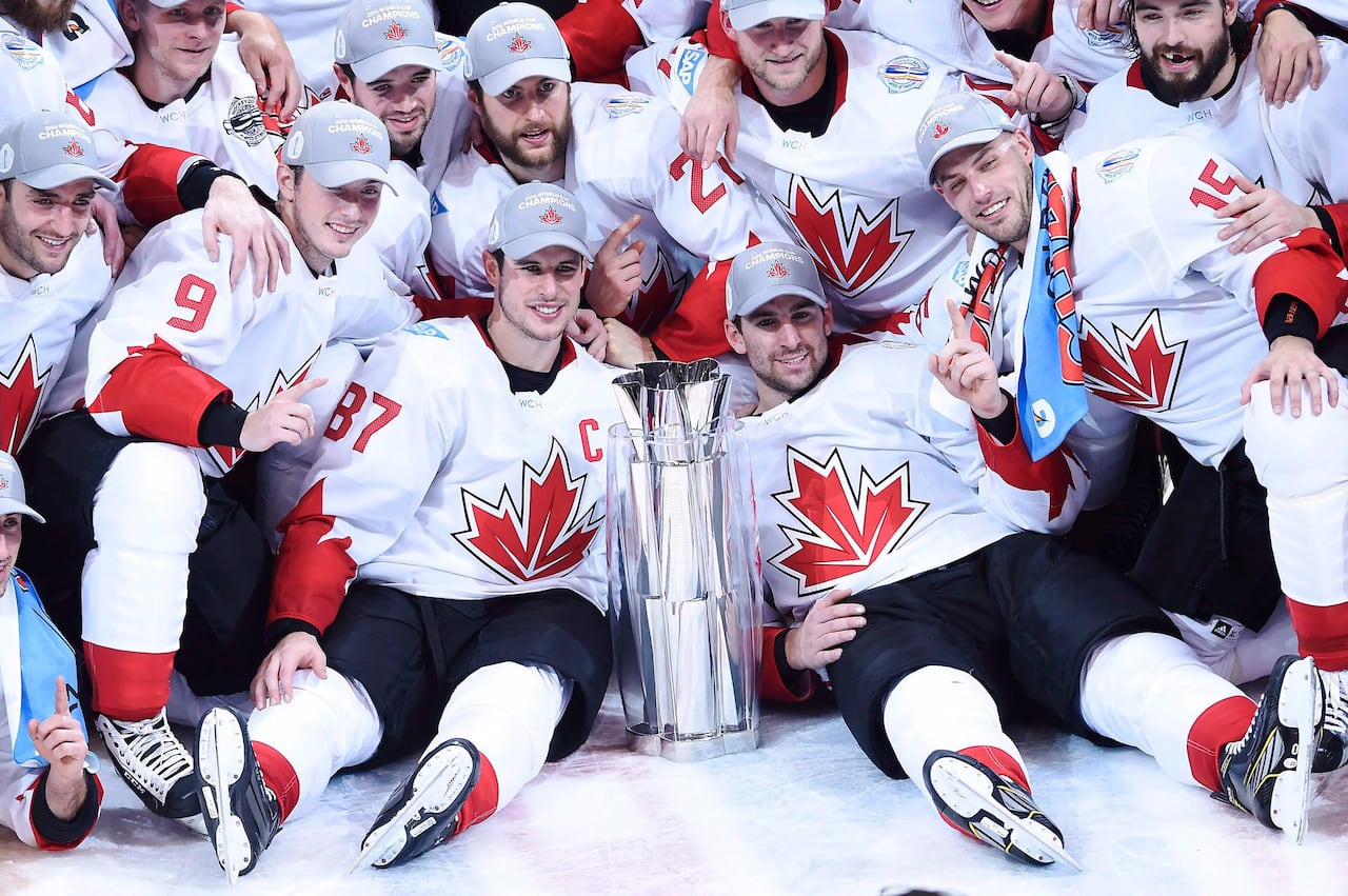 Hockey team members are seated on the ice beside a championship cup.
