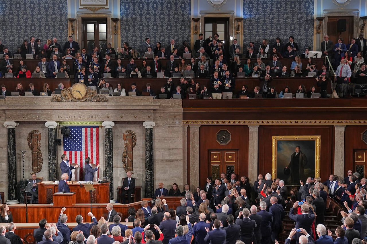 Members of the House of Representatives stand and applaud, while looking up at a group of men standing in the gallery wearing USA Olympic pullovers.