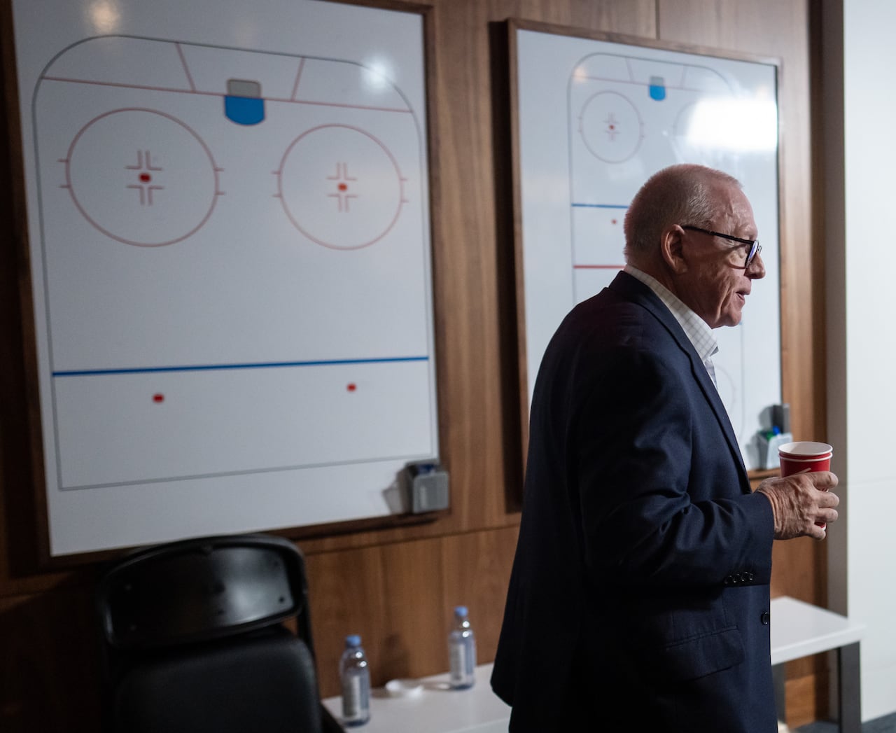 A man with coffee mugs passes two whiteboards featuring hockey strategies.