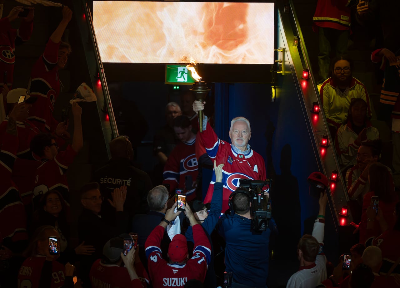 An ex-hockey athlete bears an ignited torch into a stadium before a game.