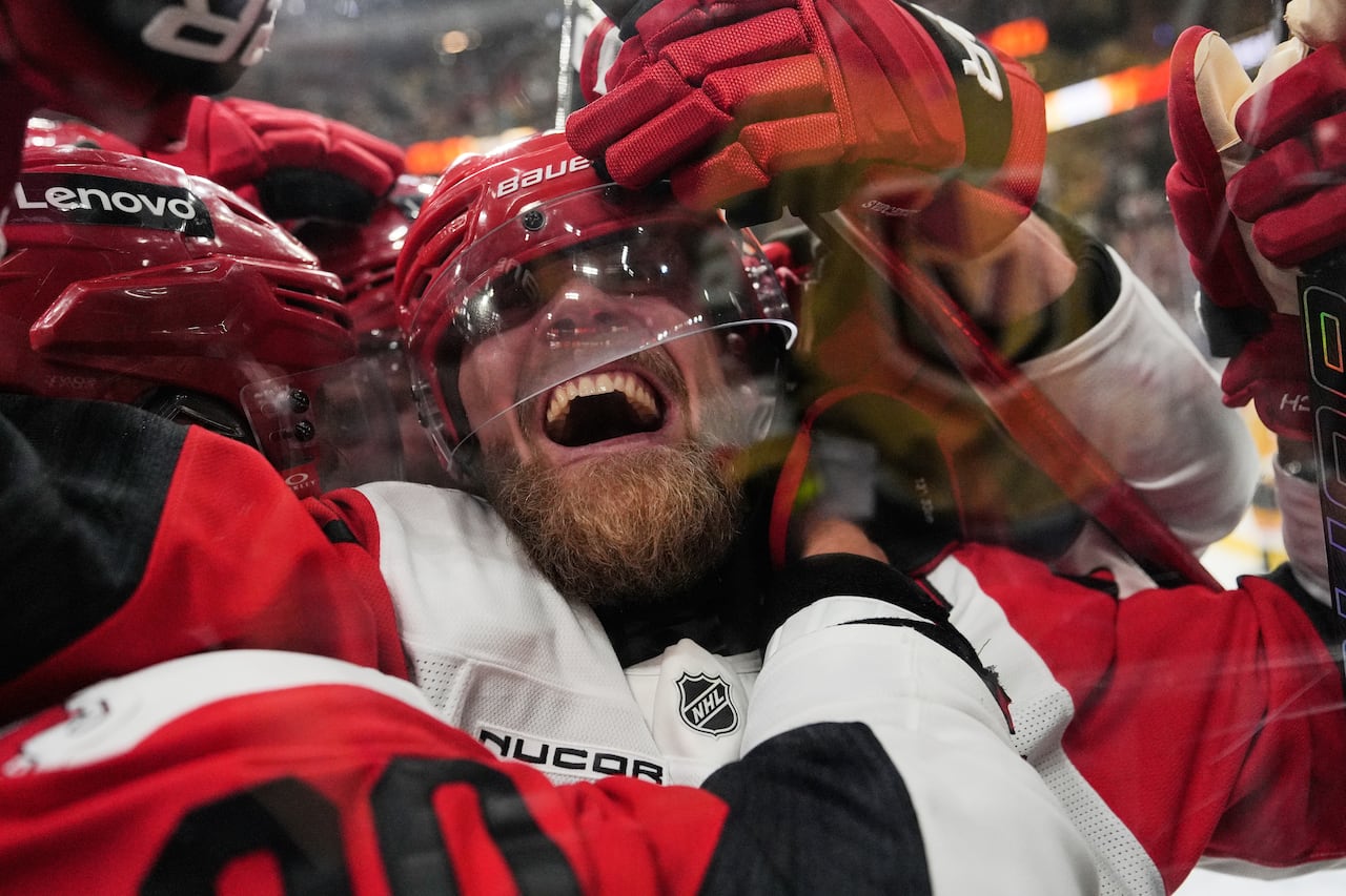 A hockey player smiles as he is mobbed by teammates celebrating a goal.