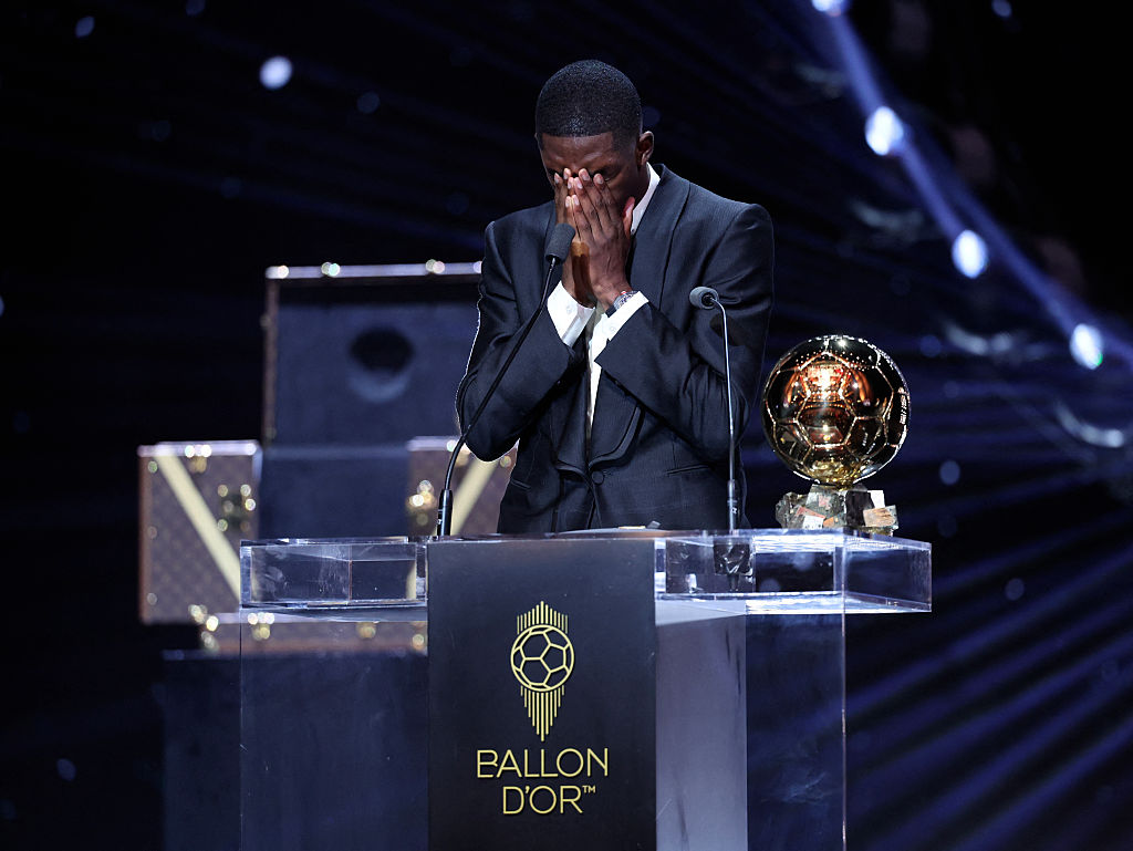 Paris Saint-Germain's French forward Ousmane Dembele reacts after receiving the Ballon d'Or award, cups face in hands.