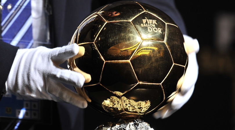 A close-up of gloved hands placing the Ballon d'Or on a perch.