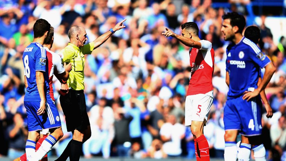 Mike Dean preparing to show a card to an Arsenal player.