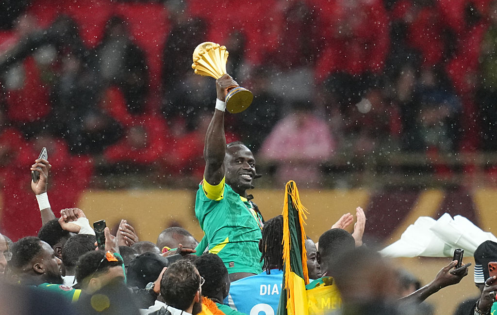Sadio Mane of Senegal lifting the AFCON trophy, being carried by team-mates, raised into the air.