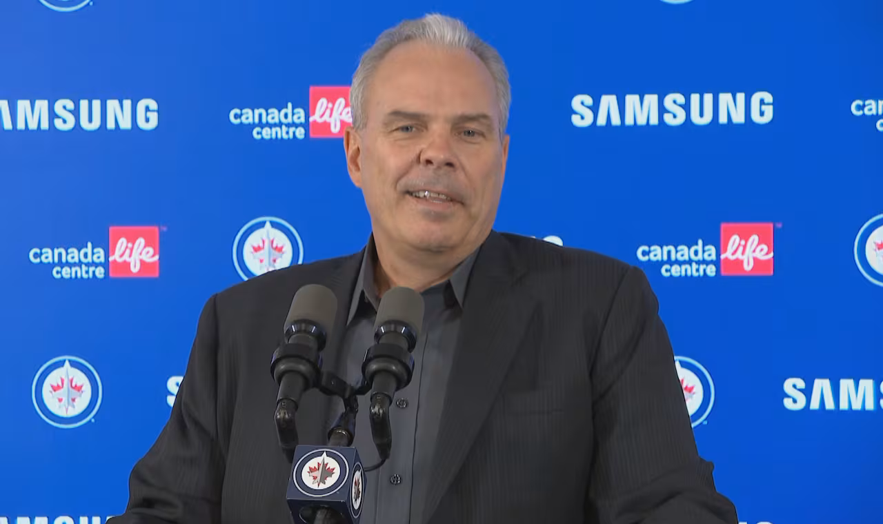 A man with grey hair stands at a podium. Behind him is a blue backdrop.